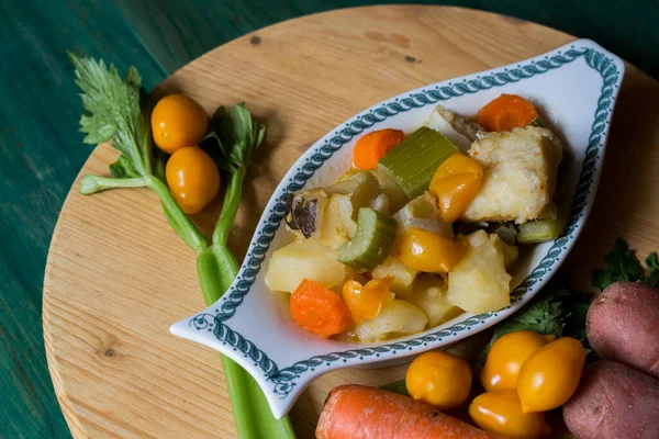 Patates, kereviz ve havuçla haşlanmış morina balığı. Tabağın yakın çekimi pişmeye hazır, yeşil ahşap arka planda.