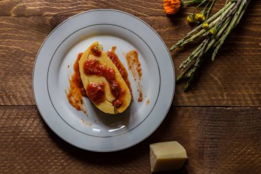 Mısır polentası kuşkonmazla sarılmış ve üzeri et suyu ve peynirle kaplı beyaz tabakta ve koyu ahşap arka planda.