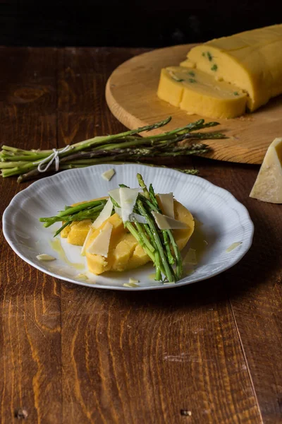 Beyaz tabakta kuşkonmaz ve peynir taneleriyle sarılmış mısır lapası ve koyu ahşap arka plan