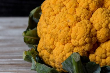 Çiğ organik turuncu karnabahar ve ahşap arka planda yeşil yapraklar.