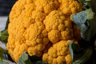 Çiğ organik turuncu karnabahar ve ahşap arka planda yeşil yapraklar.