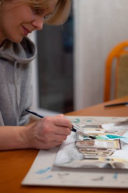 Yaratıcı sanat atölyesinin işleyişi. Ressam, fırça ve suluboya kullanarak kağıt üzerine renkli mimari şehir manzarası çiziyor