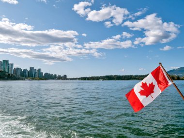 Canadian flag on blue sky and water background in Vancouver harbor.