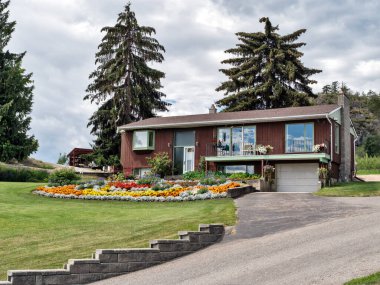 Old residential house in Canada with big flower bed on the front yard.