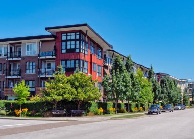 Red residential building on a street corner with cars parked beside on blue sky background