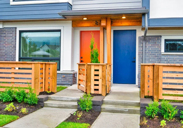 Orange and blue doors of brand new residential townhouses with wooden fence in front