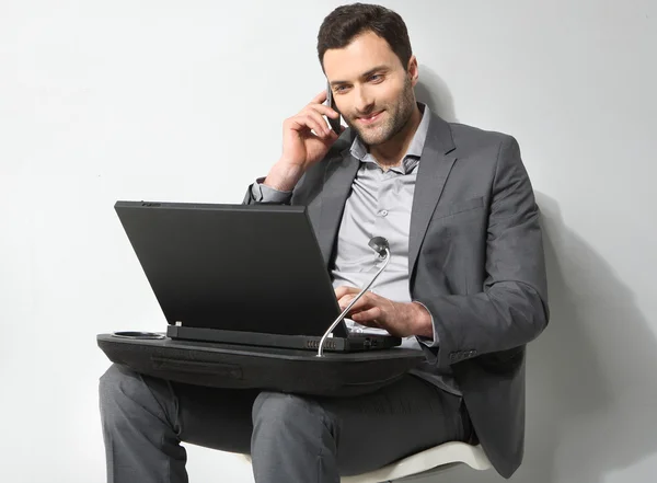 Jovem empresário falando ao telefone e trabalhando em é laptop — Fotografia de Stock