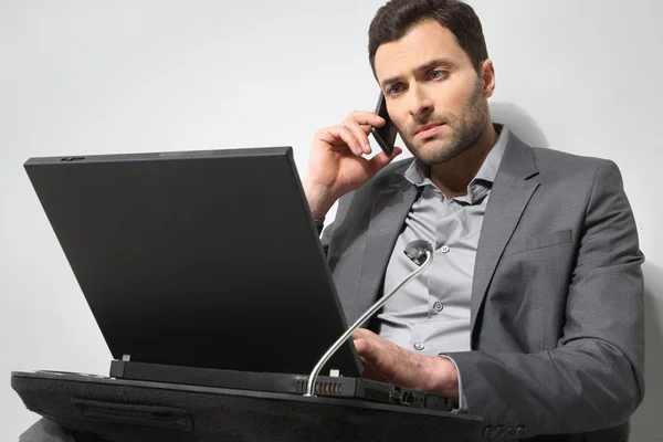 Joven hombre de negocios hablando por teléfono y trabajando en es portátil —  Fotos de Stock