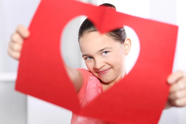 Hermosa niña mirando a través de la tarjeta con un corazón cortado —  Fotos de Stock