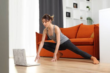 Ev egzersizleri, online eğitim. Genç bir kadın online bir eğitmenle oturma odasında antrenman yapıyor..