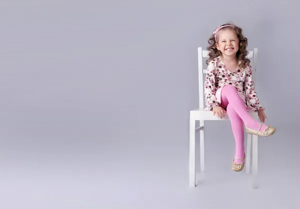 Веселая маленькая девочка сидит на стуле с улыбкой Стоковое Фото