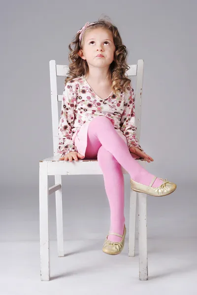 Sweet little girl sitting on the white chair, looking away, maki — Stock Photo, Image