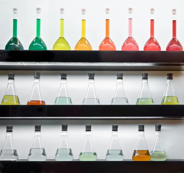 Colorful liquid in flasks laying on shelf — Stock Photo, Image