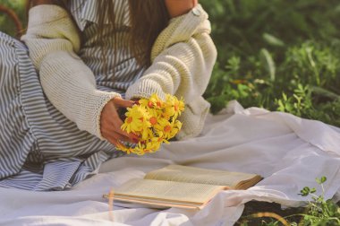 Yazlık elbiseli genç kız elinde bir buket sarı papatya tutuyor ve yaz günü parkta tek başına kitap okuyor. Uzayı metin için kopyala. Rahatlayın ve dinlenin.