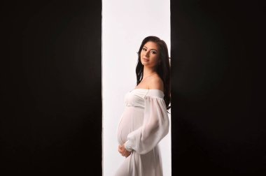 Hamile karnını tutan beyaz elbiseli güzel hamile kadın siyah beyaz arka planda izole edilmiş. Bebek bekliyormuş. Metin için alanı kopyala