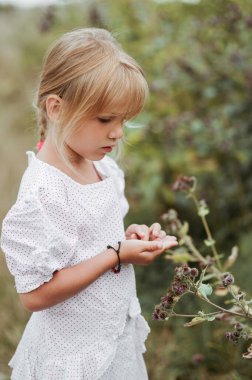 Yazın kırsalda elinde devedikeni çiçekleri tutan beyaz puantiyeli bir kızın portresi. Retro tarzı, çocukluk