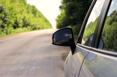 Kırsal yol arka planına sahip arabanın ayna tarafının görüntüsü. Seyahat konsepti