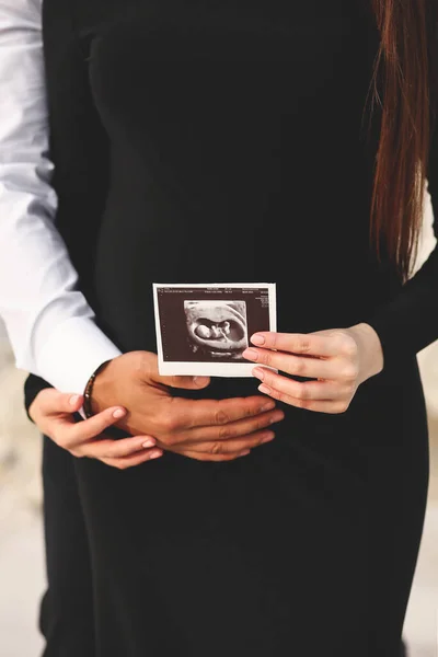 孕妇和丈夫手拉手放在怀孕腹部的特写照片和胎儿超声波照片 爱的概念 家庭概念 — 图库照片
