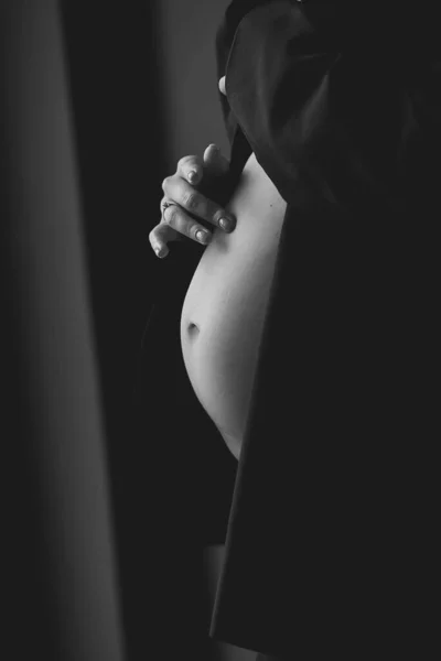 穿着黑色夹克的孕妇在黑色背景下触摸腹部的黑白照片 爱的概念 怀孕28周 祝你怀孕愉快 — 图库照片
