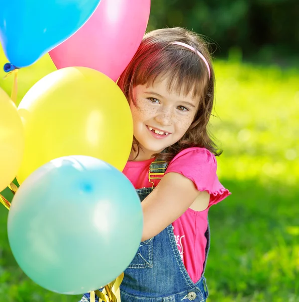 Menina feliz segurando balões coloridos no parque verde — Fotografia de Stock