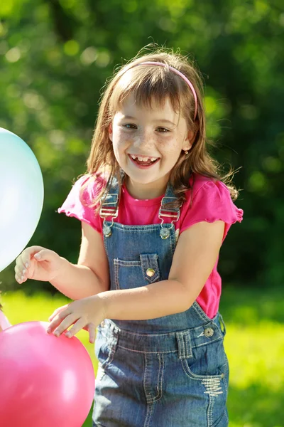 Menina feliz segurando balões coloridos no parque verde — Fotografia de Stock