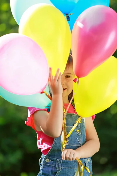 Little happy girl holding colorful balloons in green park — Stock Photo, Image