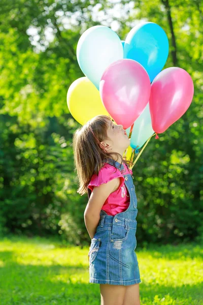 Liten glad tjej med färgglada ballonger i grön park — Stockfoto