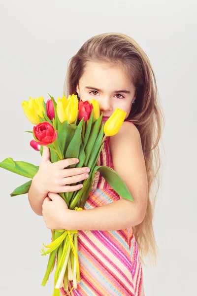 Mooi meisje met eerlijke haren in een roze jurk houdt bloemen — Stockfoto