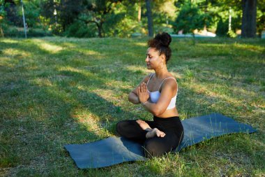 Yeşil ağaçların arasında egzersiz yapan genç ve güzel bir kadının görüntüsü. Sabahları açık hava savaşçısı yoga pozu alıştırması yapıyorum.