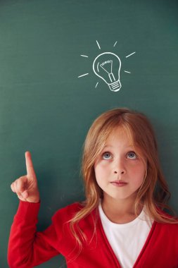 School child (girl) in classroom. Funny kid against green chalkboard. Idea and creativity concept. Copyspace on background. Back to school concept. 