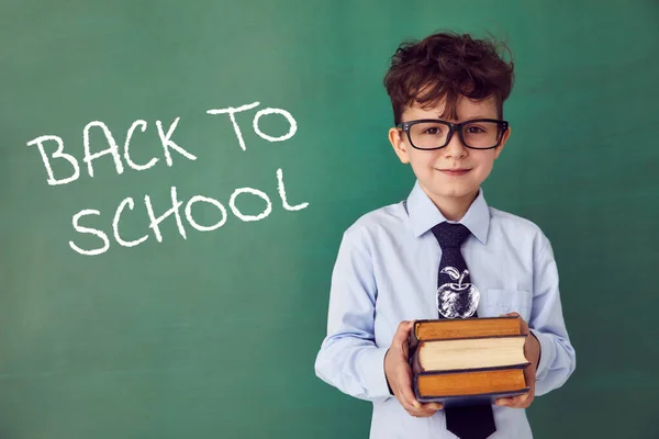 School child (boy) in classroom. Funny kid against green chalkboard. Idea and creativity concept. Copyspace on background. Back to school concept.