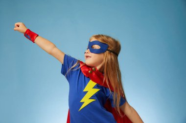 Kırmızı yağmurluk giyen komik, küçük süper kahraman çocuk. Mavi arka plana karşı komik çocuk. Fikir ve yaratıcılık kavramı.