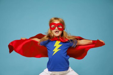 Kırmızı yağmurluk giyen komik, küçük süper kahraman çocuk. Mavi arka plana karşı komik çocuk. Fikir ve yaratıcılık kavramı.