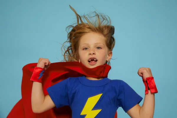 赤いレインコートを着た面白い小さなパワースーパーヒーローの子供 女の子 青を背景にした面白い子だ アイデアと創造性の概念 — ストック写真
