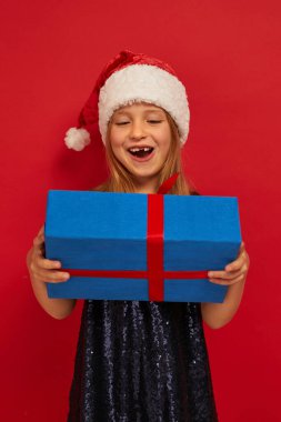 Noel Baba kırmızı şapkalı, elinde hediye kutusuyla gülümseyen komik çocuk. Noel konsepti. Red Backgroun 'a ateş etmek