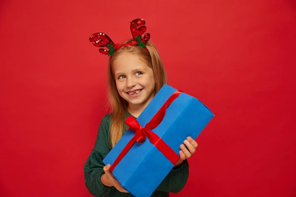 在驯鹿发带笑有趣的孩子 手里拿着圣诞礼物圣诞节的概念在红色背景下射击 — 图库照片