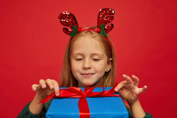 在驯鹿发带笑有趣的孩子 手里拿着圣诞礼物圣诞节的概念在红色背景下射击 — 图库照片