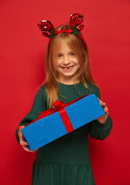 在驯鹿发带笑有趣的孩子 手里拿着圣诞礼物圣诞节的概念在红色背景下射击 图库图片