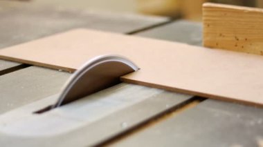 Marangoz ahşap işçisi atölyede mobilya yapmak için endüstriyel elektrikli odun kesme makinesiyle odun kesiyor.