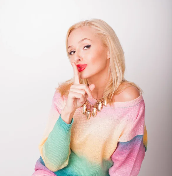 The beautiful fresh blonde the girl in a bright jacket and with red lips on a white background looks in a shot and fingers shows silently — Stock Photo, Image