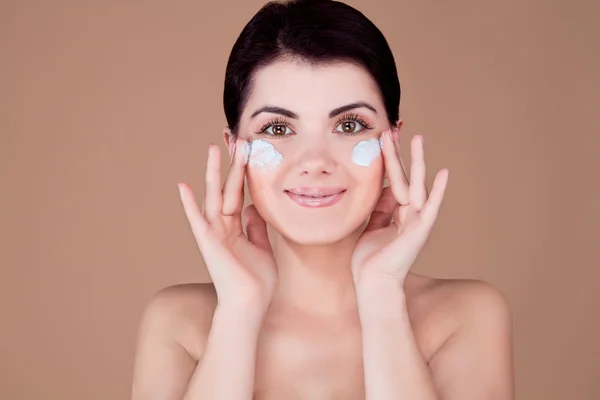 Ragazza con crema sulle guance sorridente con entrambe le mani vicino al viso — Foto Stock