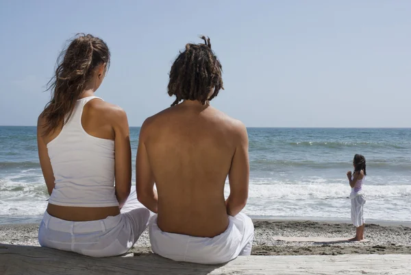 Vue arrière d'un couple regardant une femme faire du yoga sur la plage Photos De Stock Libres De Droits