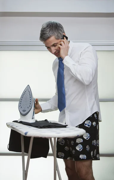 Empresario hablando en un teléfono móvil mientras plancha pantalones Imagen de stock