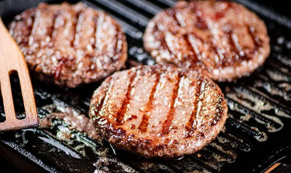 Cooking a delicious grilled burger on a pan with oil bubbles. On a black background. High quality photo