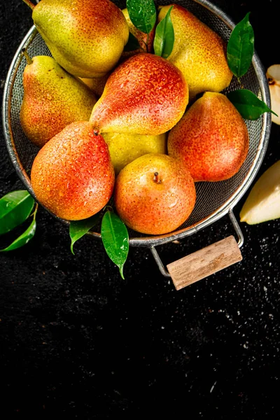 Fresh pears with leaves in a colander. On a black background. High quality photo