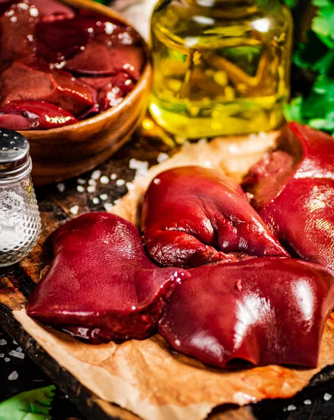 Pieces of raw liver with spices, oil and herbs. Against a dark background. High quality photo