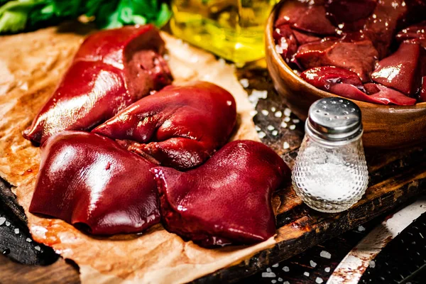 Pieces of raw liver with spices, oil and herbs. Against a dark background. High quality photo