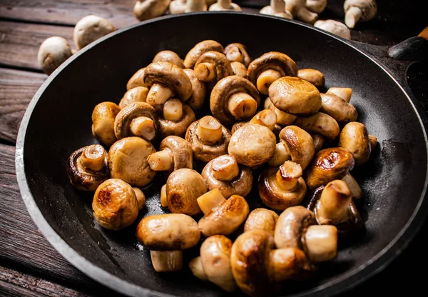 Delicious small fried mushrooms in a frying pan. On a wooden background. High quality photo