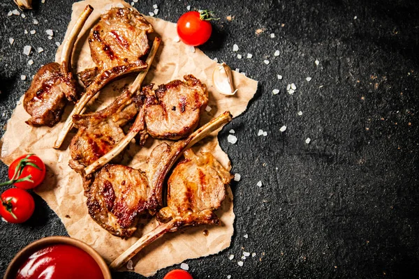 Grilled lamb rack on paper with tomato sauce and cherry tomatoes. On a black background. High quality photo