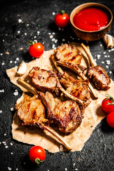Grilled lamb rack on paper with tomato sauce and cherry tomatoes. On a black background. High quality photo